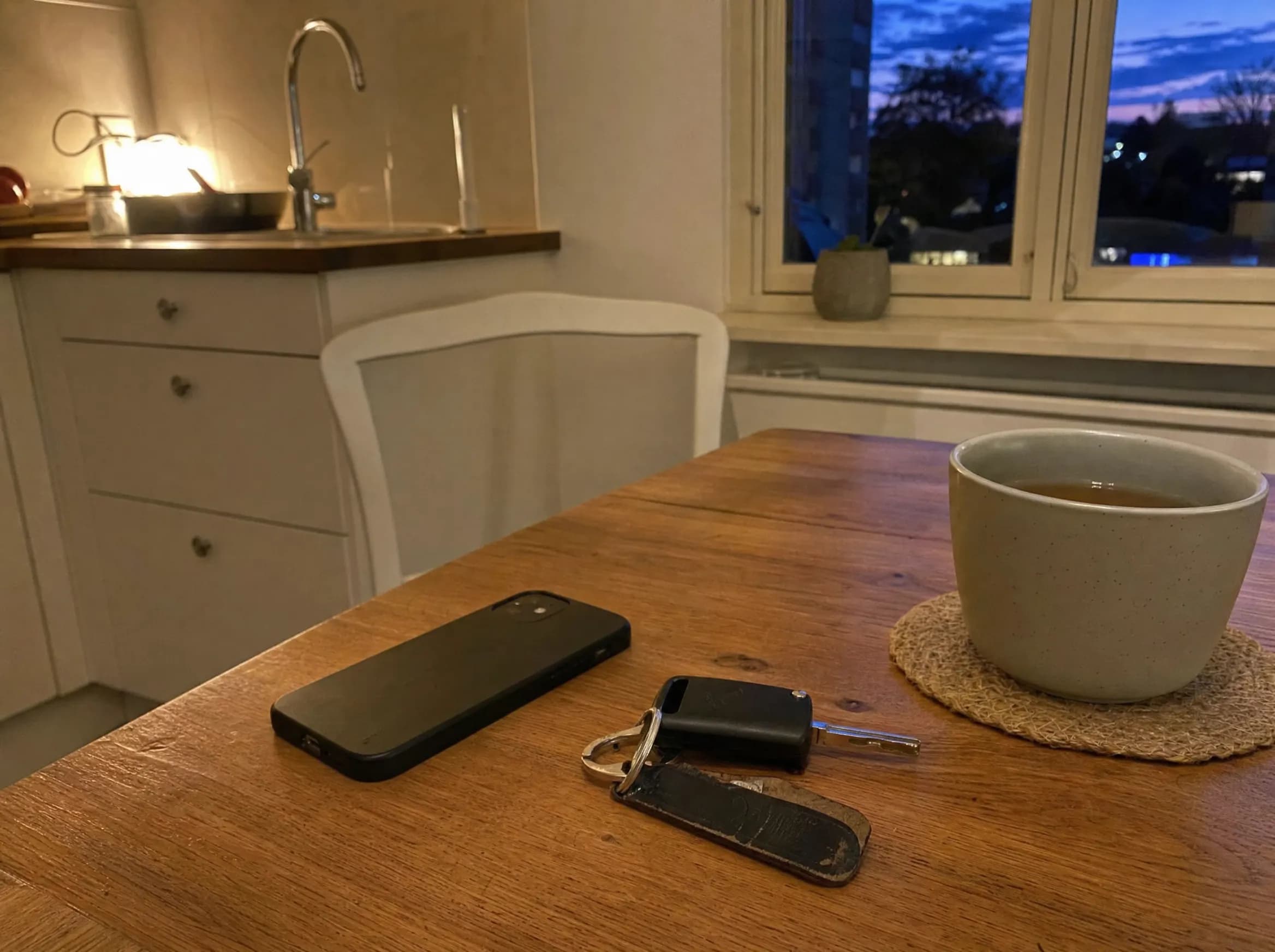 Handy liegt umgedreht neben Autoschlüssel und Tee